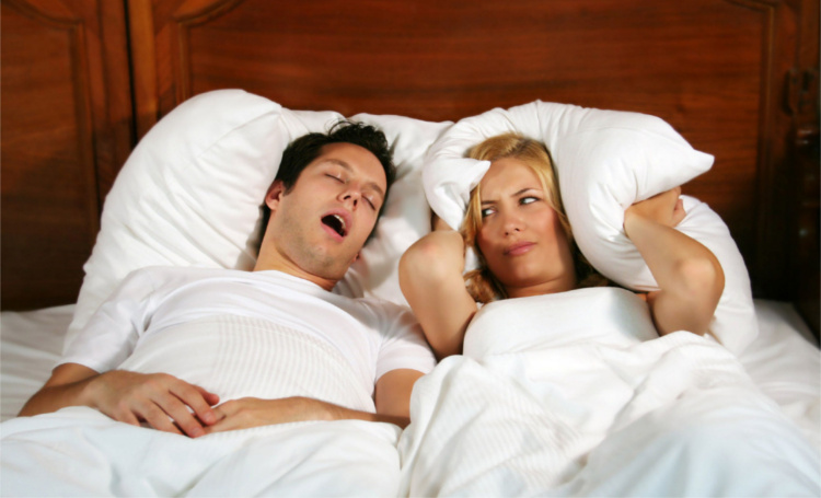 Couple in bed while the woman is trying to sleep and the man is snoring. Shutterstock