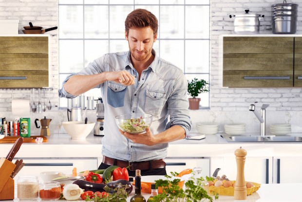 Handsome man cooking at home preparing salad in kitchen.